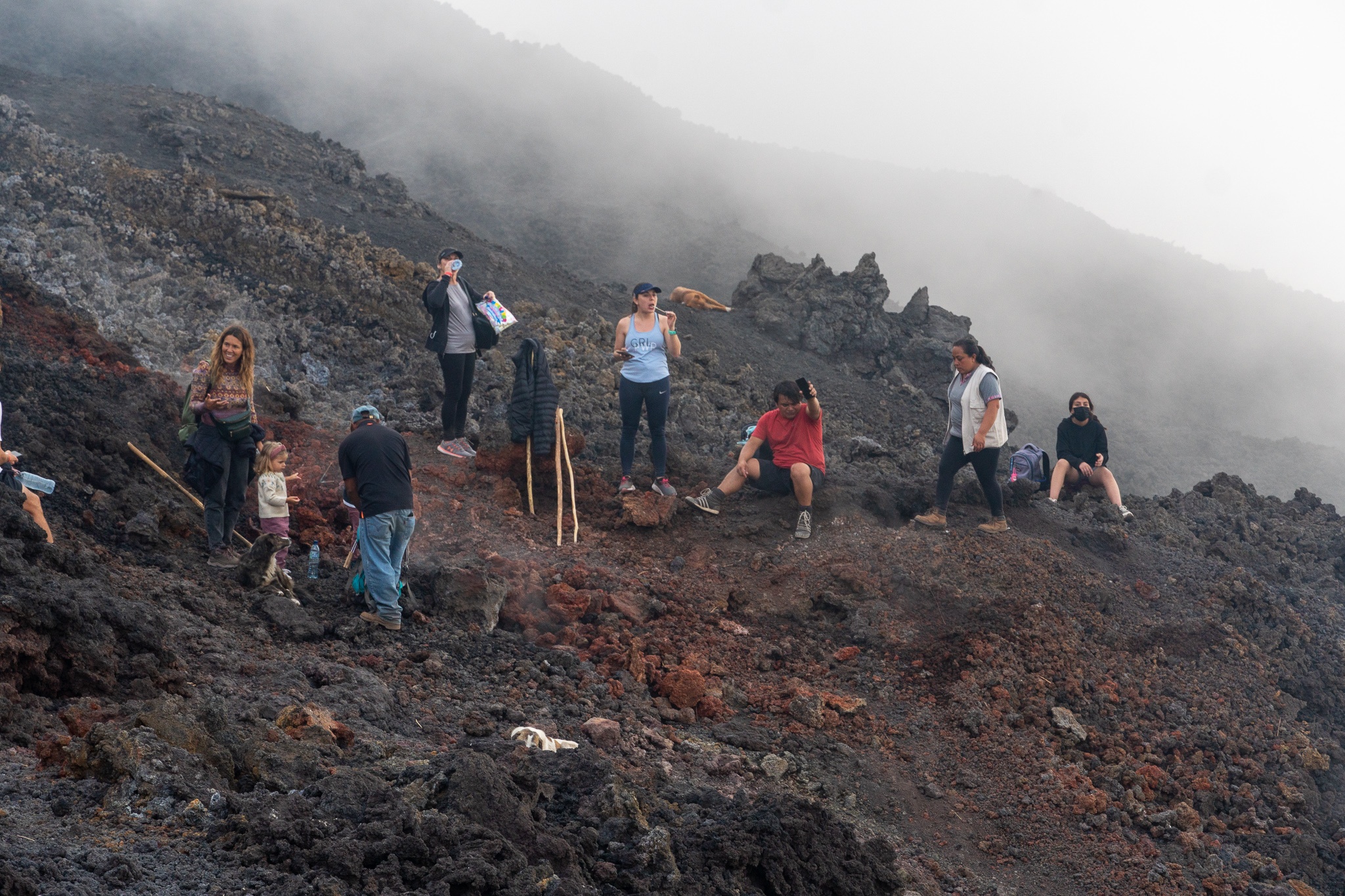 A group of people stand in front of a smoking volcano