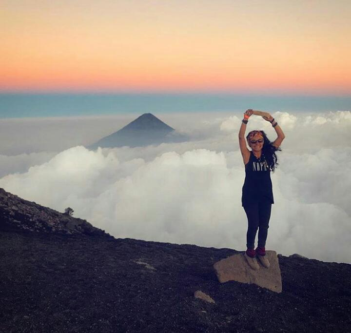 Christa Castillo posing above the clouds with a volcano in the background