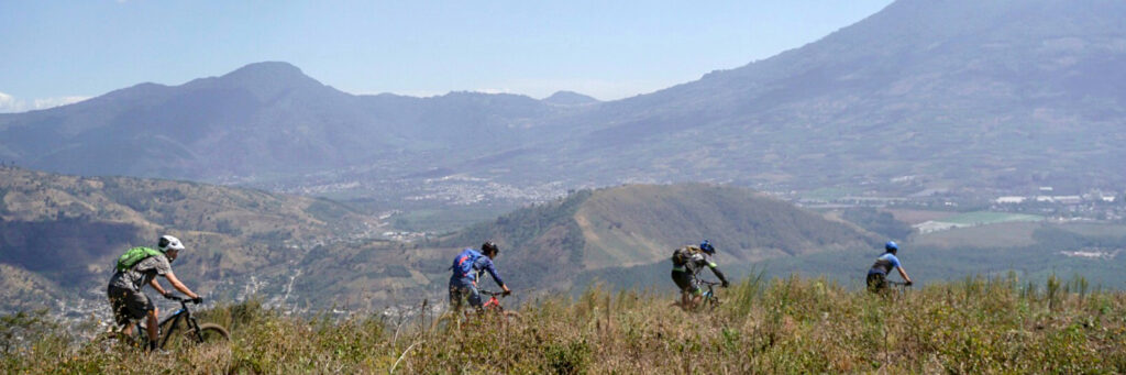Mountain bikers riding from left to right with Guatemala mountains in the background