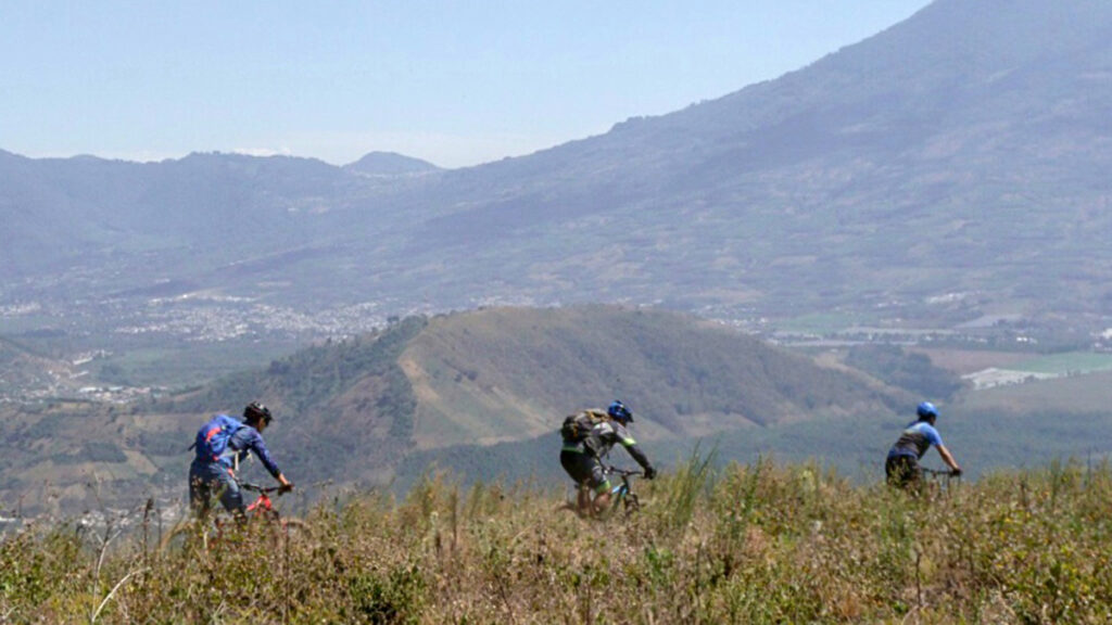 Mountain bikers riding from left to right with Guatemala mountains in the background