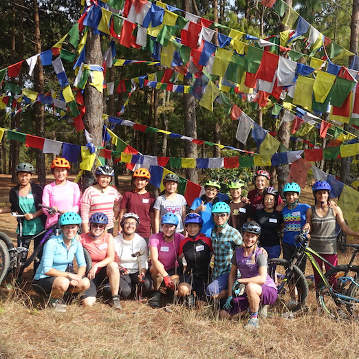 A group shot of mountain bikers in front of some flags in Nepal