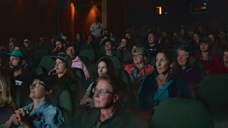 An audience sits in a dark movie theatre at a World Ride movie night